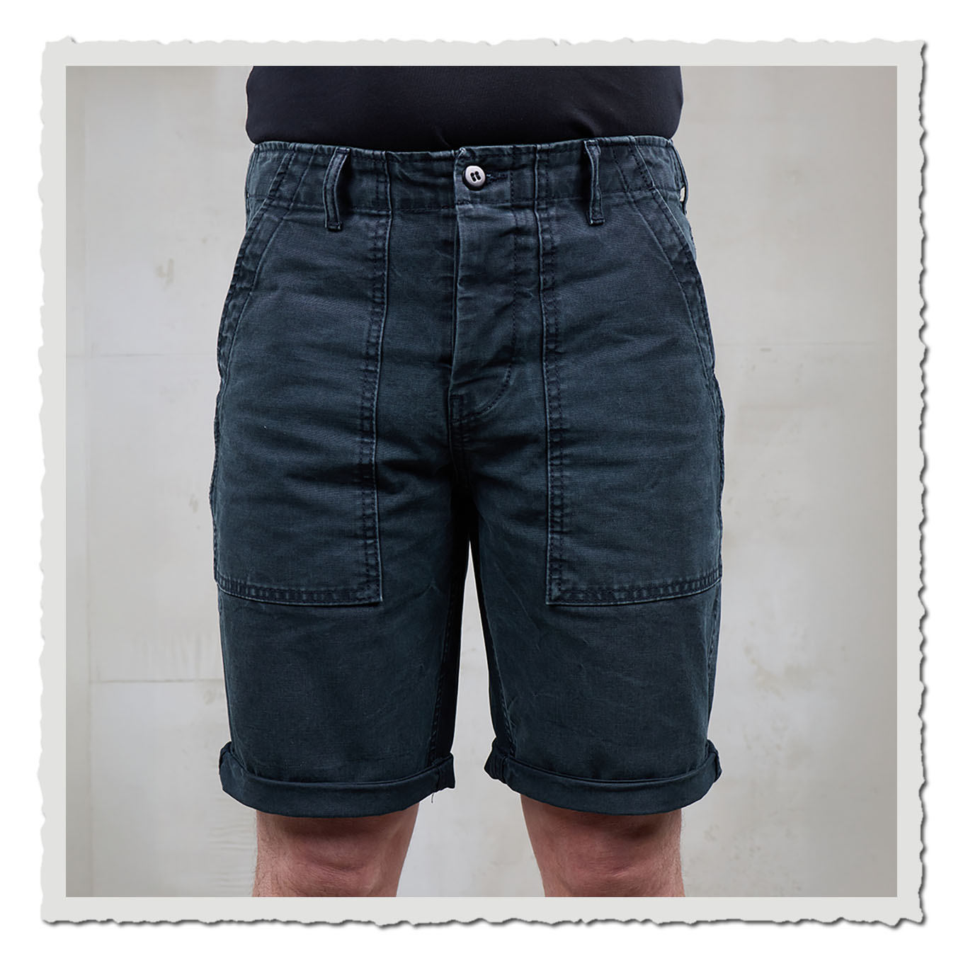 Dunkle Shorts von vorn getragen, vor hellem Hintergrund mit neutraler Studiowand.